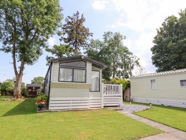 A mobile home with a small porch and a lawn with trees at Woodlands Lodge in Bontuchel near Ruthin
