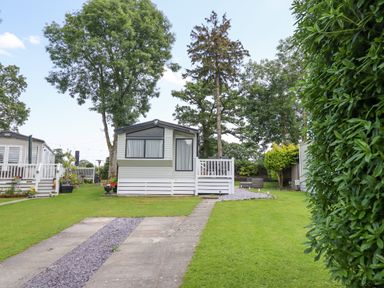 A caravan on a grass plot with a paved pathway and trees surrounding at Woodlands Lodge in Bontuchel near Ruthin