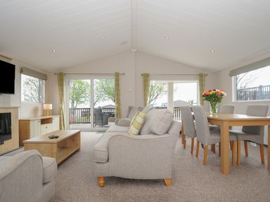 A living room with grey sofas a wooden coffee table dining table with chairs and flowers on the table at Lodge 67 at Riviera Bay Coastal Retreat in Brixham