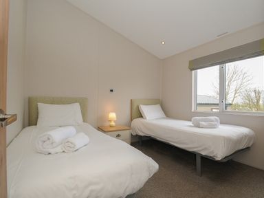 A bedroom with two single beds bedside table with lamp and a window at Lodge 67 at Riviera Bay Coastal Retreat in Brixham
