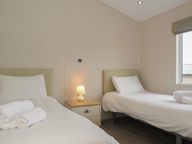 A bedroom with two single beds a nightstand with a lamp and a window at Lodge 67 at Riviera Bay Coastal Retreat in Brixham
