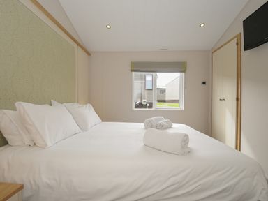 A bedroom with a large bed topped with rolled towels a window a wardrobe and a wall-mounted TV at Lodge 67 at Riviera Bay Coastal Retreat Brixham