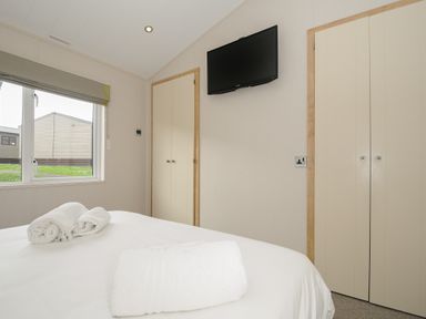 A bedroom with a bed with white towels on it a window and a wall mounted television at Lodge 67 at Riviera Bay Coastal Retreat in Brixham