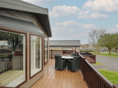 An outdoor deck with a table and four chairs next to a building with large windows at Lodge 67 at Riviera Bay Coastal Retreat in Brixham
