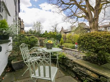An outdoor patio area with metal table and chairs surrounded by plants and stone walls at Acorn Cottage in Windermere