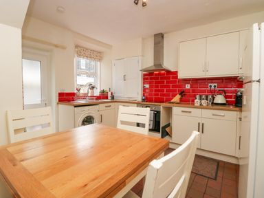 A kitchen with white cabinets red tiled backsplash wooden dining table and white chairs at Acorn Cottage in Windermere