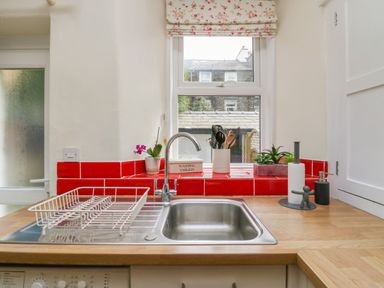 A kitchen sink with a drying rack and utensil holder under a window with floral blinds at Acorn Cottage in Windermere