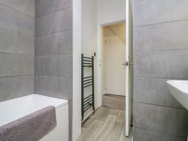A bathroom with a bathtub towel radiator and sink at Acorn Cottage in Windermere