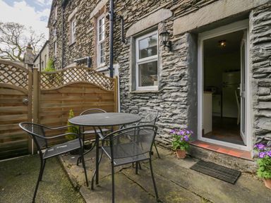 An outdoor patio with a round metal table and four chairs next to a stone wall and wooden fence at Acorn Cottage in Windermere