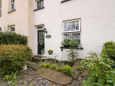 The exterior of a house with a black door a window with plants on the sill a round metal table with two chairs and plants in front at Acorn Cottage in Windermere