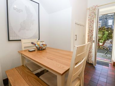 A dining area with a wooden table chairs bench a basket with snacks and an open door leading to a garden at Acorn Cottage in Windermere