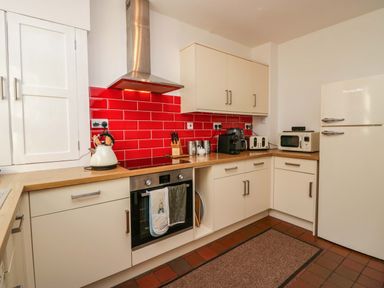 A kitchen with white cabinets red tiled backsplash stainless steel oven and hood kettle toaster microwave and fridge at Acorn Cottage in Windermere