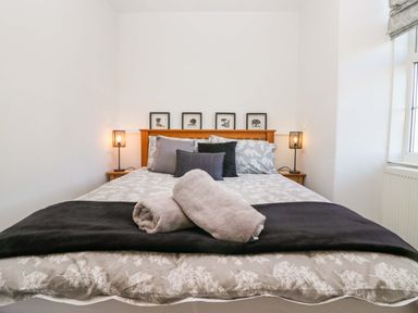 A bedroom with a bed with patterned bedding and rolled towels on it at Acorn Cottage in Windermere