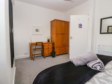 A bedroom with a wooden desk and chair a wooden wardrobe a bed with towels on it and a mirror on the wall at Acorn Cottage in Windermere