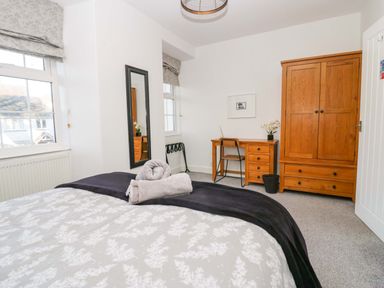 A bedroom with a bed folded towels a wooden wardrobe and desk with a chair at Acorn Cottage in Windermere