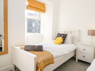 A bedroom with a white bed a bedside table with a lamp and a window with an orange blind at Acorn Cottage in Windermere