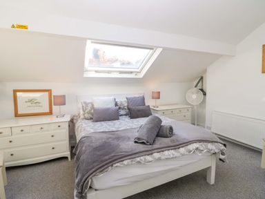 A bedroom with a bed under a skylight window two bedside tables with lamps a fan and framed pictures at Acorn Cottage in Windermere
