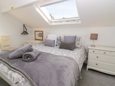 A bedroom with a bed by a skylight window with bedside tables lamps and a chair at Acorn Cottage in Windermere
