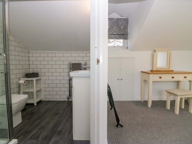 A bathroom with a toilet and shower on the left and a room with a dressing table and stool on the right at Acorn Cottage in Windermere