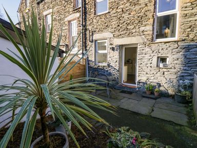 An outdoor stone patio area with potted plants and a stone building wall with windows and an open door at Acorn Cottage in Windermere