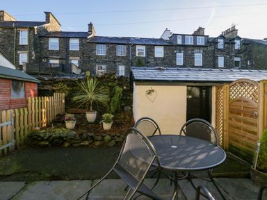 A backyard with a metal table and chairs a small garden shed plants and stone wall at Acorn Cottage in Windermere