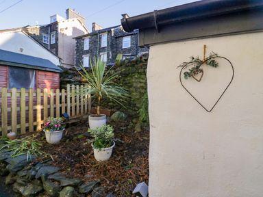 A small garden area with potted plants a wooden fence a stone wall and a red shed at Acorn Cottage in Windermere