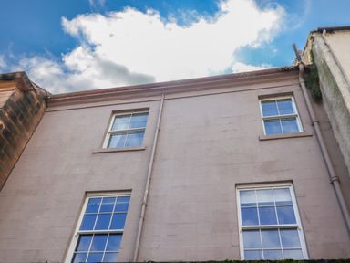 Exterior wall of a building with four windows and drainpipes under a blue sky with clouds at The Wizards Chamber in Alnwick