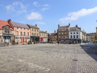A cobblestone square with historic buildings and outdoor seating at The Wizard's Chamber in Alnwick