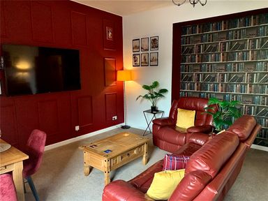 A living room with red leather sofas wooden coffee table plants and a television mounted on a red wall at The Wizard's Chamber in Alnwick