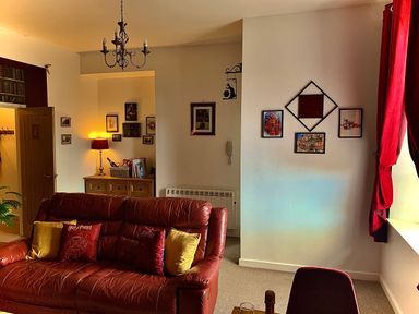 A living room with a leather sofa pillows wall art and a wooden cabinet with a lamp at The Wizard's Chamber in Alnwick