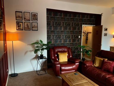 A room with red leather chairs and sofa a wooden coffee table plants a floor lamp framed pictures and books wallpaper at The Wizard's Chamber in Alnwick