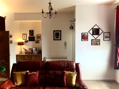 A living room with a brown leather sofa with cushions two sets of framed pictures on walls and a wooden sideboard with a lamp at The Wizards Chamber in Alnwick
