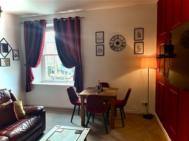 A living room with leather sofa red curtains dining table with four chairs and a floor lamp at The Wizard's Chamber in Alnwick