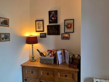 A wooden sideboard with a table lamp a basket of snacks framed pictures and decorative items on top at The Wizards Chamber in Alnwick