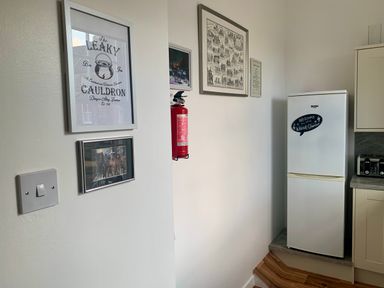 A kitchen corner with a refrigerator a fire extinguisher framed pictures and a toaster on the counter at The Wizard's Chamber in Alnwick