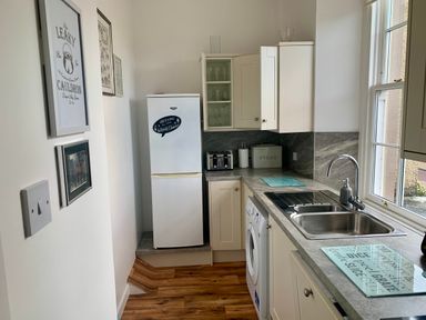 A kitchen with white cabinets a white refrigerator a toaster a bread box a washing machine and a stainless steel sink at The Wizard's Chamber in Alnwick