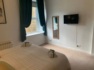 A bedroom with a bed, window with curtains, wall-mounted TV, and a mirror at The Wizards Chamber in Alnwick