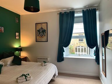 A bedroom with a bed a window with dark curtains wall decorations and a bedside table with a lamp at The Wizards Chamber in Alnwick