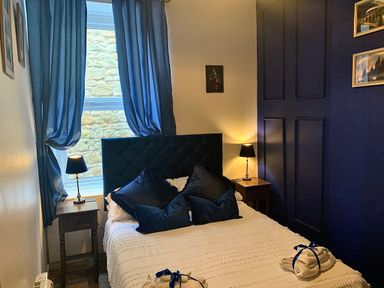 A bedroom with a bed between two bedside tables with lamps and blue curtains at The Wizard's Chamber in Alnwick