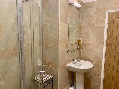 A bathroom with a corner shower enclosure a pedestal sink a mirror and a wooden door at The Wizard's Chamber in Alnwick