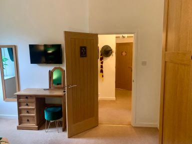 A bedroom with a wooden desk and mirror a mounted TV an open wooden door showing a hallway with a hat and scarf hanging at The Wizard's Chamber in Alnwick