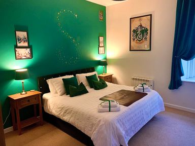 A bedroom with a double bed green accent wall bedside tables and lamps at The Wizards Chamber in Alnwick