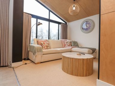 A living room with a beige sectional sofa near large windows and a round wooden coffee table at Encil Gyfrinfa in Gwynus near Llithfaen