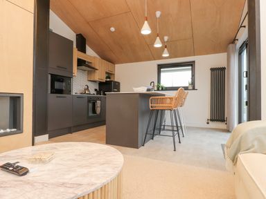 A kitchen area with an island and bar stools next to a window and a table with a remote control at Encil Gyfrinfa in Gwynus near Llithfaen