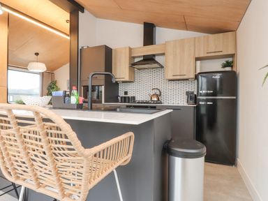 A kitchen with a black fridge and sink with two wicker chairs at Encil Gyfrinfa in Gwynus near Llithfaen