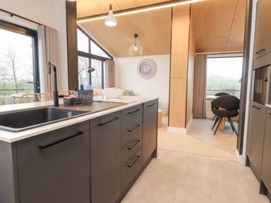 A kitchen with a black sink and cabinets next to a dining area with black chairs at Encil Gyfrinfa in Gwynus near Llithfaen