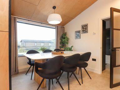 A dining room with six black chairs around a rectangular table and a large window at Encil Gyfrinfa in Gwynus near Llithfaen