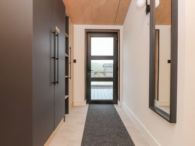 A hallway with a black door at the end a large mirror on the right wall and dark cabinets on the left at Encil Gyfrinfa in Gwynus near Llithfaen