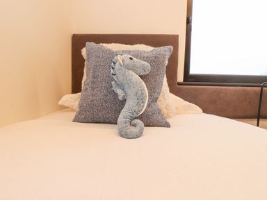 A bed with pillows and a stuffed seahorse toy near a window at Encil Gyfrinfa in Gwynus near Llithfaen