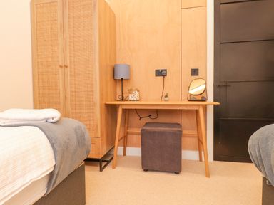 A bedroom with a wooden desk a brown ottoman lamp mirror and a wooden wardrobe at Encil Gyfrinfa in Gwynus near Llithfaen